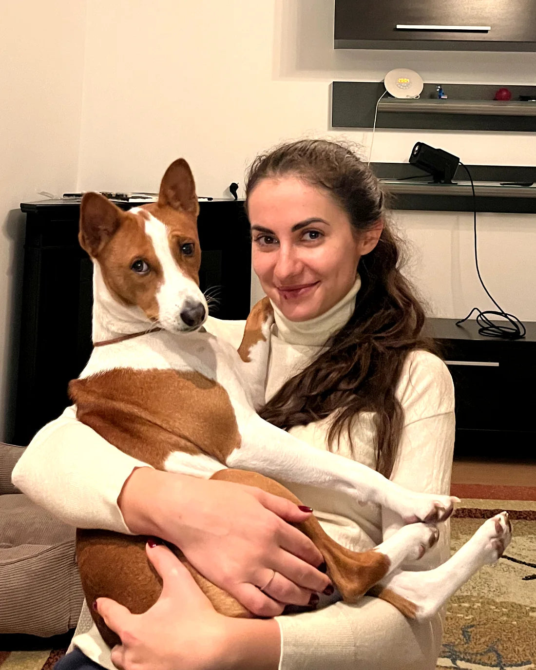 Ana sitting on the living-room floor holding Jack, her red-and-white Basenji, relaxed across her lap.